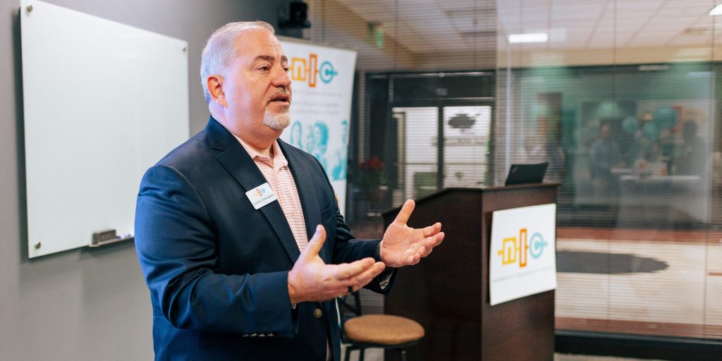 Charlie Imbergamo, CEO of the Nonprofit Leadership Center (a white male with grey hair and a grey beard wearing a navy blue suit) speaks to nonprofit leaders and board members