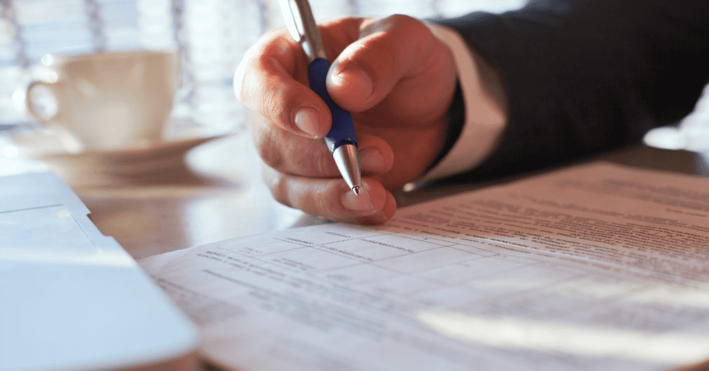 Photo of a man's hand that appears to be white wearing a dark-colored suit holding a pen and looking at photos