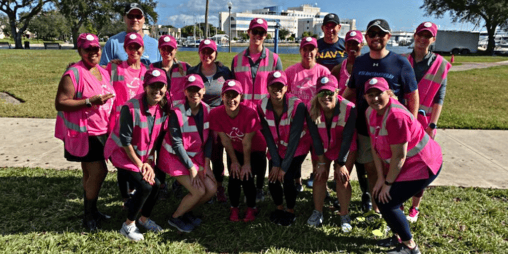 Girls on the Run event committee, featuring a large group of men and women wearing pink shirts in a park