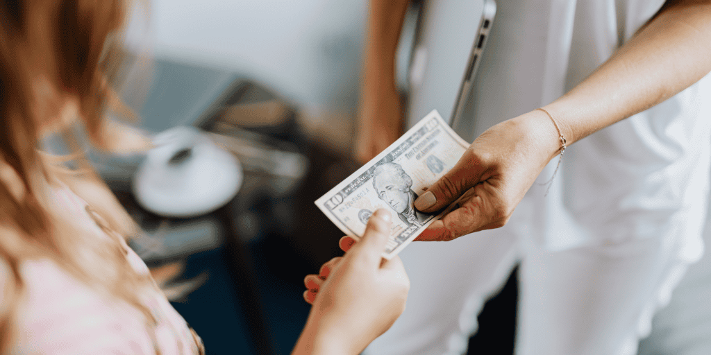 Two white women one giving a $10 bill to the other as donation