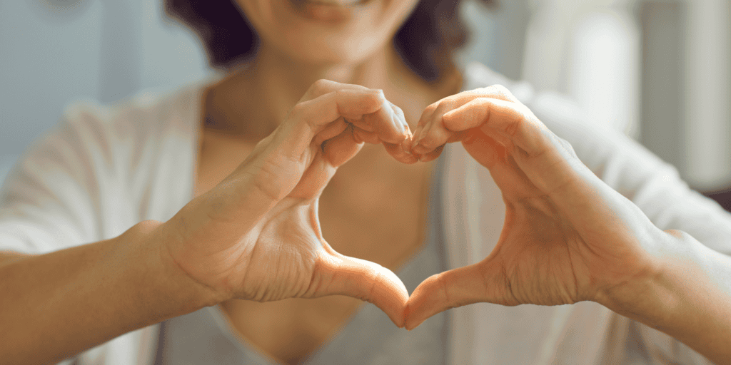 A white woman making the shape of her heart with her hands