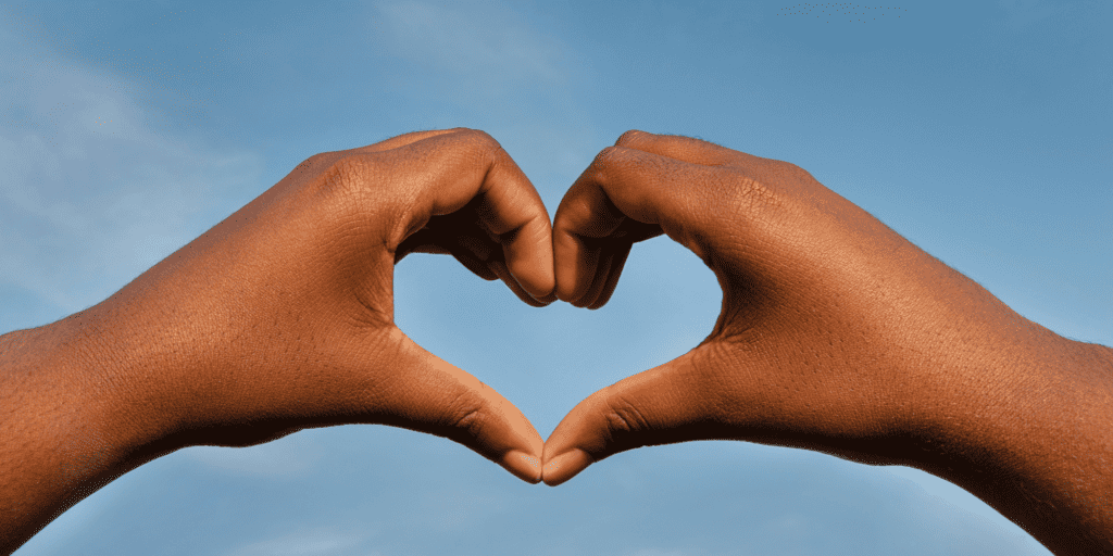 Image of two black hands forming a heart shape against a sky background