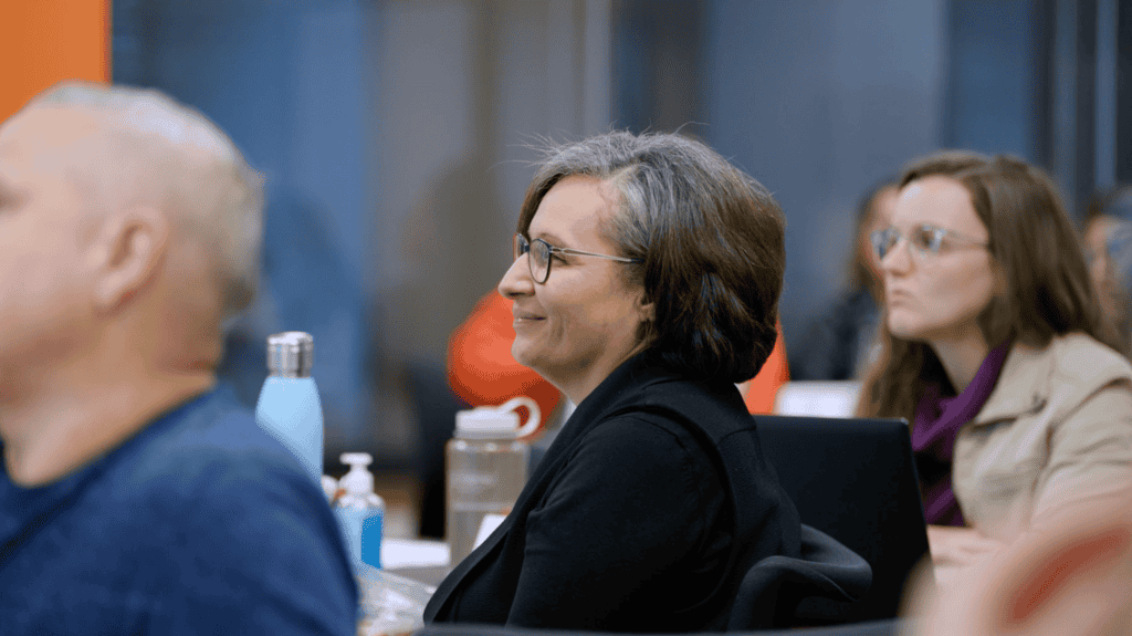 Angie Montes, a woman with light skin and short grey hair sitting in the NLC trainer center, smiling as she learns with other nonprofit leaders