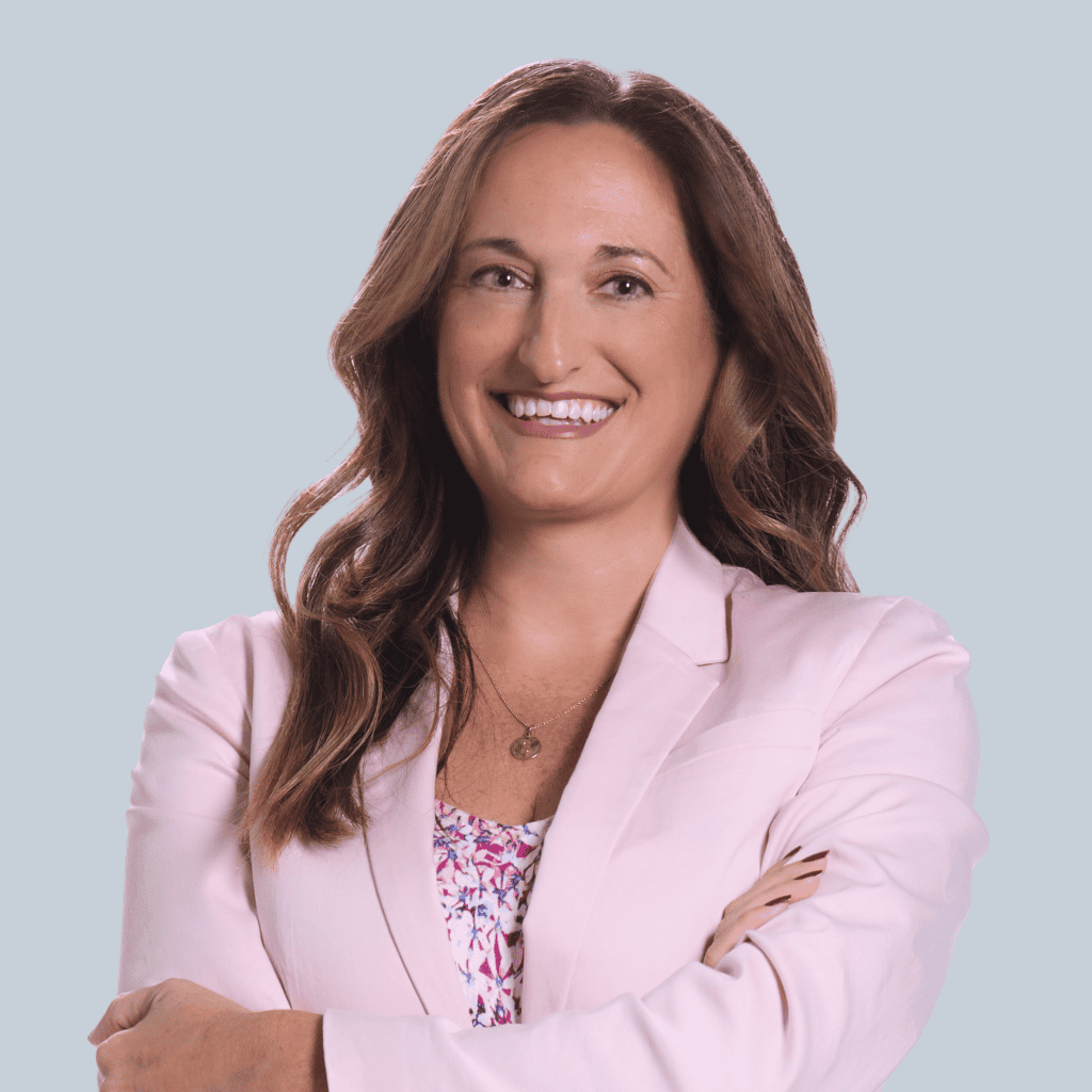 Photo of Katie Shultz, a white woman with long brown hair wearing a pink suit and smiling into the camera