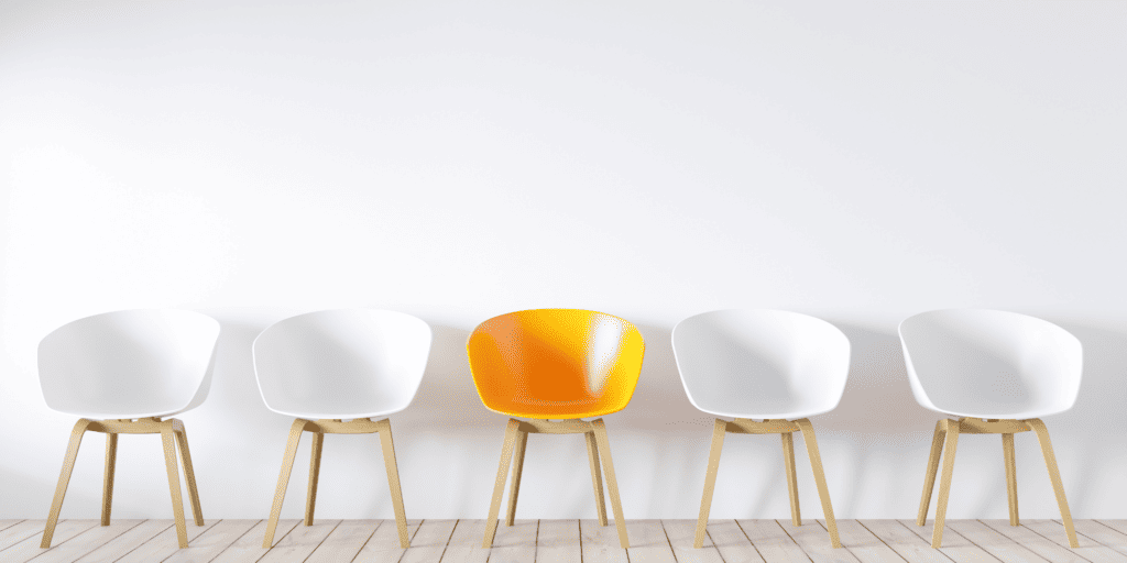 Five chairs in a line, four are white and the middle one is orange, all against a white background