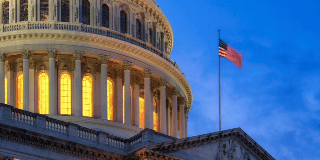 Image of the top of the US Capitol at night with the American flag waving in the wind