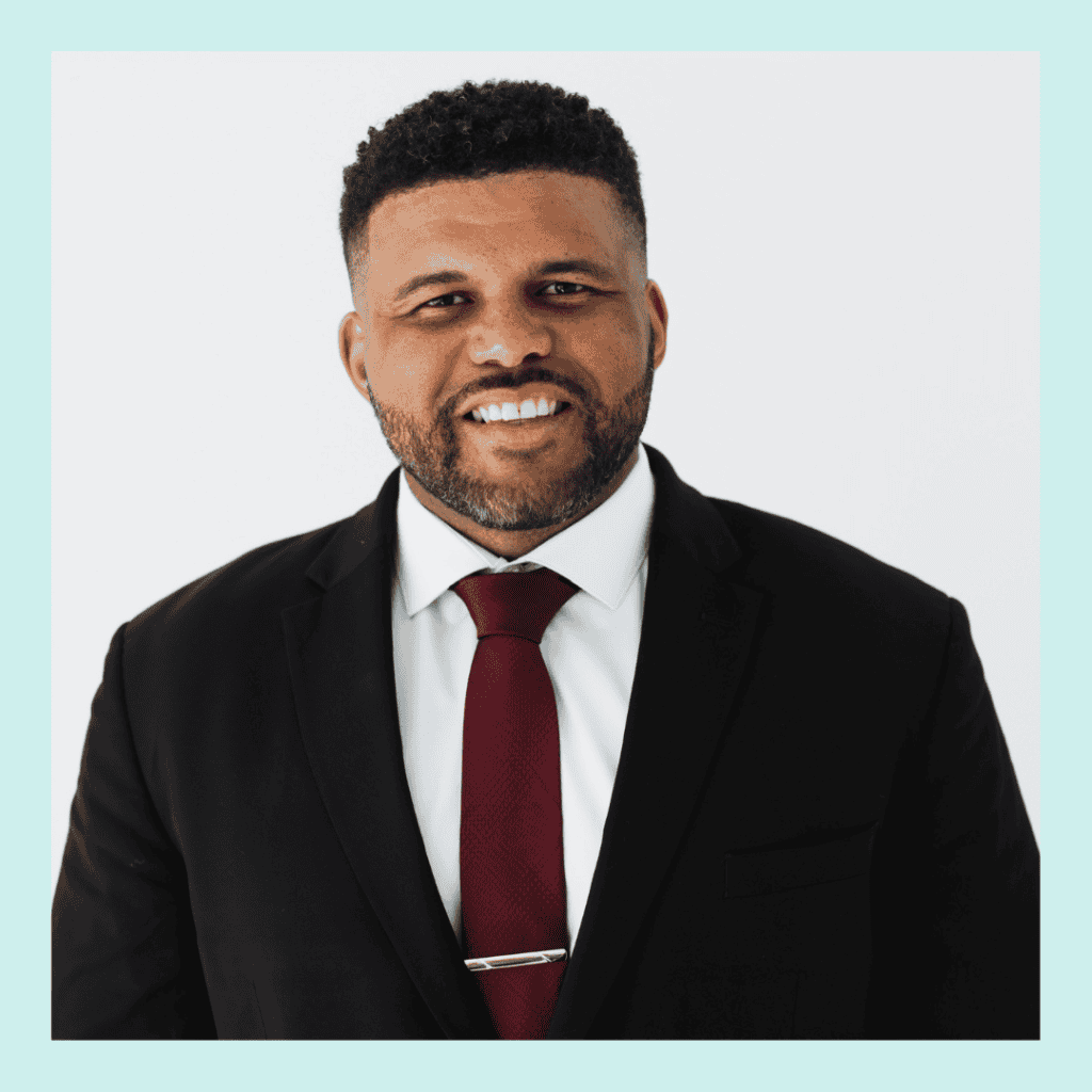 Professional headshot smiling man in a black suit white shirt and red tie with a gold tie bar against a light background