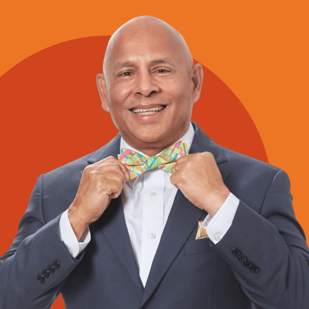 Luis R. Visot, a Hispanic man wearing a green and pink bowtie and a dark grey suit jacket against a red and orange background