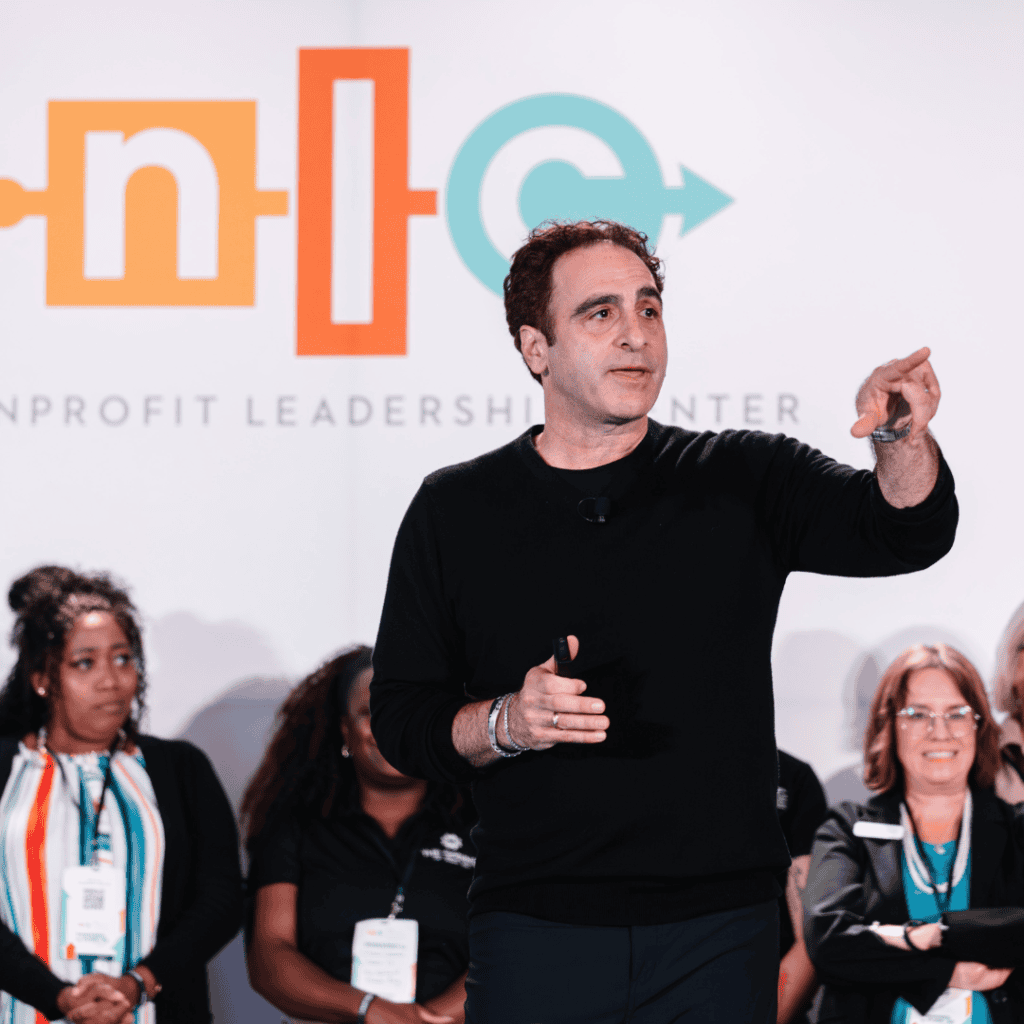 Matt 2 Nonprofit Leadership Center of Tampa Bay Male speaker in a black sweater gesturing on stage at a nonprofit leadership event with audience members in the background