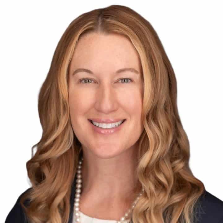 Smiling professional woman with shoulder length blonde hair wearing a pearl necklace and dark blazer head and shoulders portrait