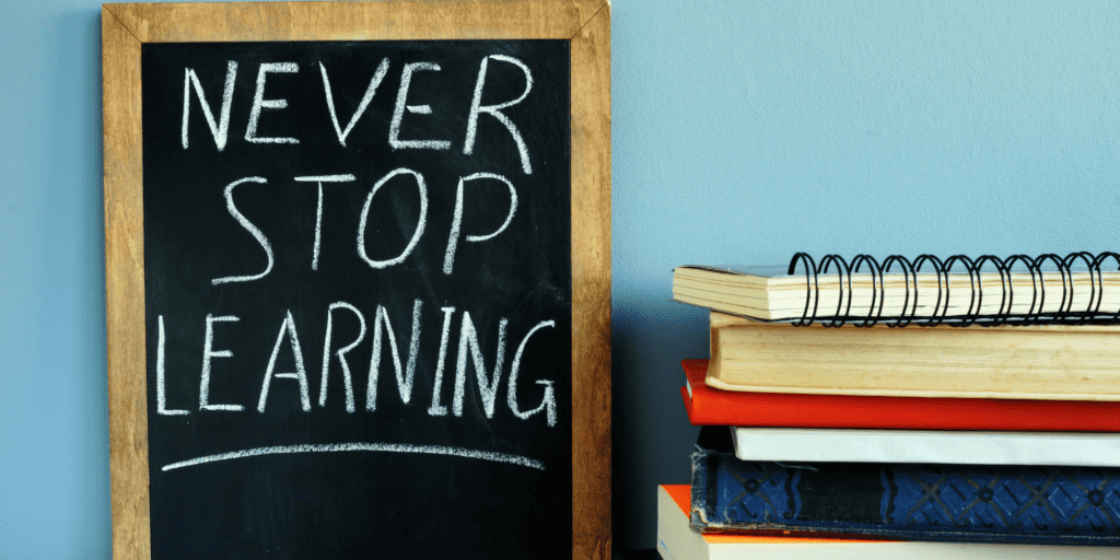 A chalkboard that says Never Stop Learning next to a stack of notebooks and books