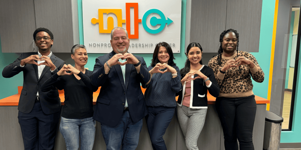 A photo of all members of the Nonprofit Leadership Center Staff Team, looking at the camera and making a heart with their hands. This includes six individuals that are diverse in age, gender, race and ethnicity.