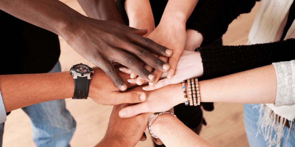 A group of diverse hands representing many different skin tones staked on top of each other in unity