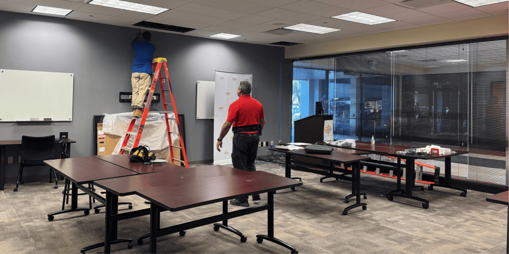 Image of NLC's Tampa training center with two workers adding tech features into the ceiling