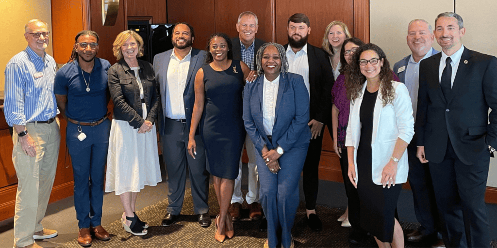8 professionals of diverse genders, races, ethnicities and ages stand smiling alongside professors and leaders to graduate from the Certificate in Nonprofit Leadership at the University of Tampa, in collaboration with the Nonprofit Leadership Center