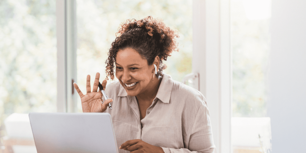 Black woman waving at her computer screen while smiling