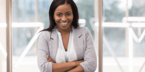 Nonprofit Leadership Center of Tampa Bay A Black woman is standing in front of a window wearing a white top and grey jacket with her arms crossed smiling in to the camera