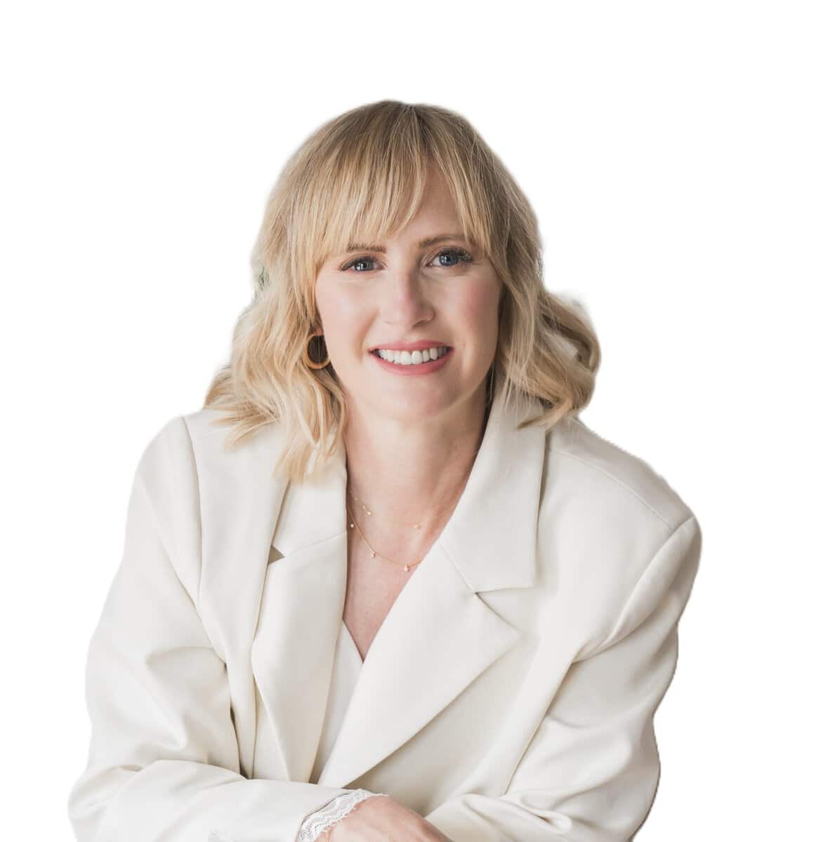Smiling blonde woman in a white blazer posing for a professional portrait against a white background