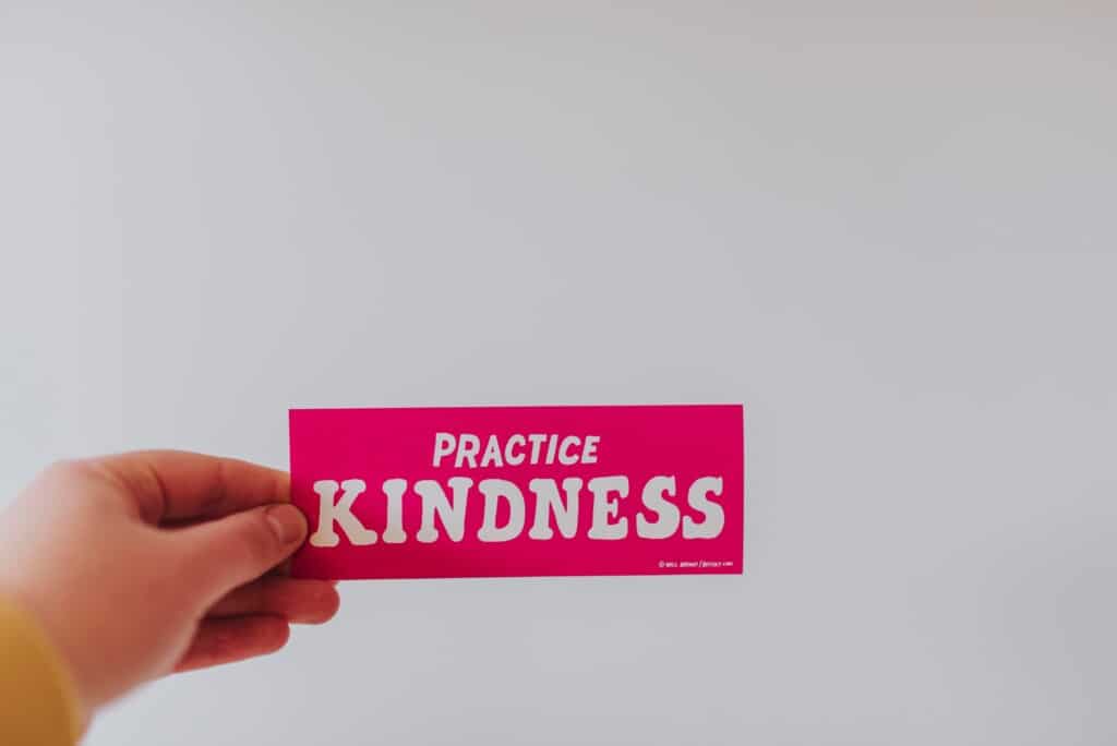 A white hand holding a pink slip of paper that says "Practice kindness."