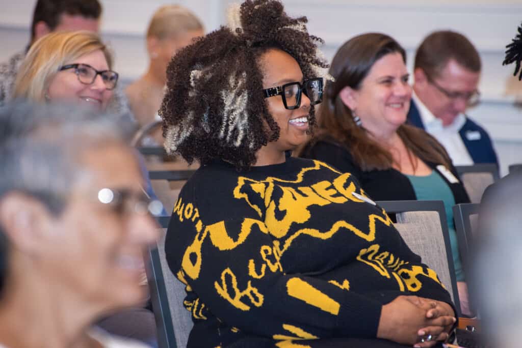 A group of nonprofit leaders in a professional development session watching a trainer, with the focus on a Black woman wearing a yellow and black top