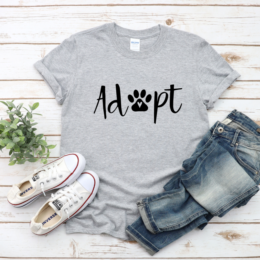 Grey T-shirt that says adopt in black type, with the "o" being a paw with a heart in the center